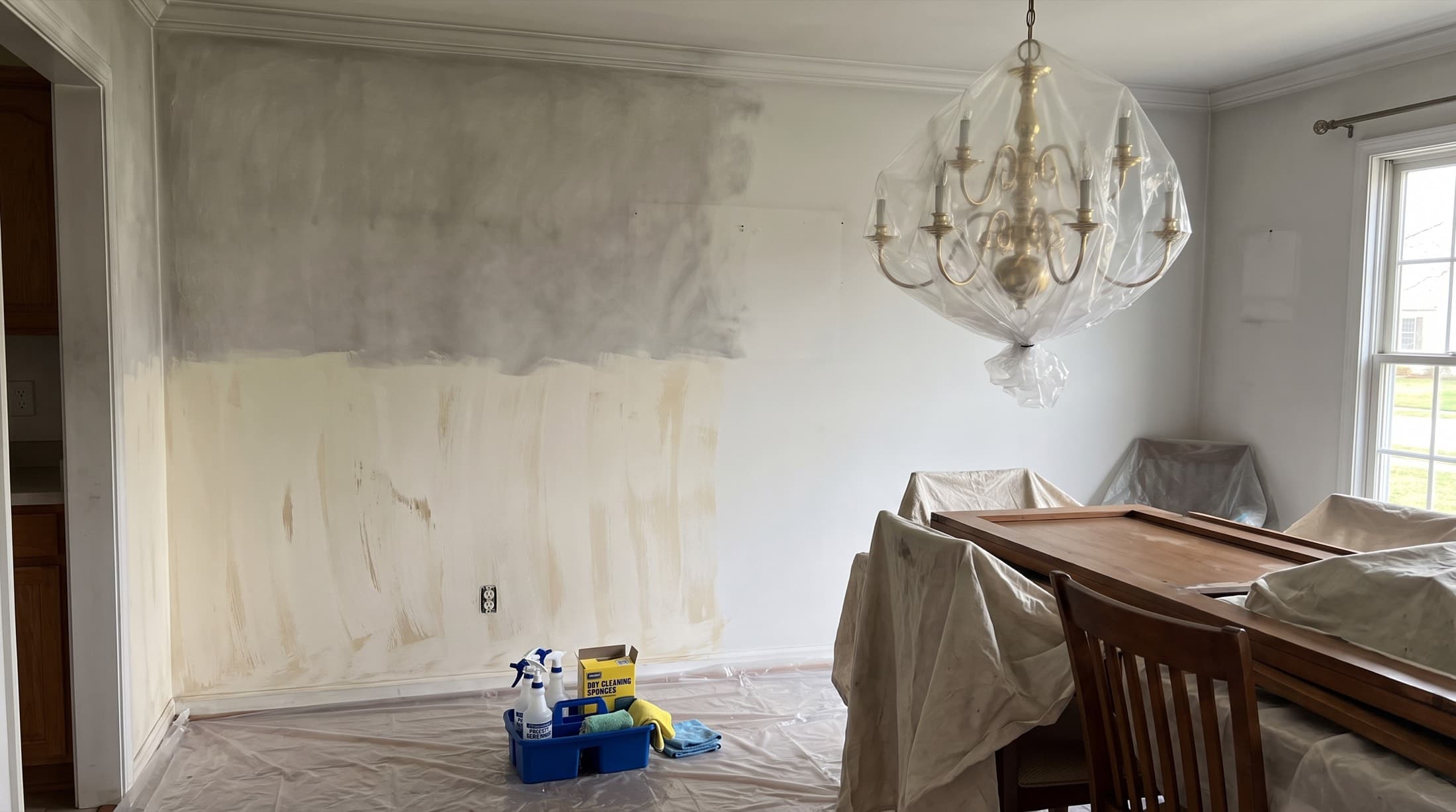 A dining room wall half-cleaned of soot — gray smoke haze above, clean paint and sponge strokes below