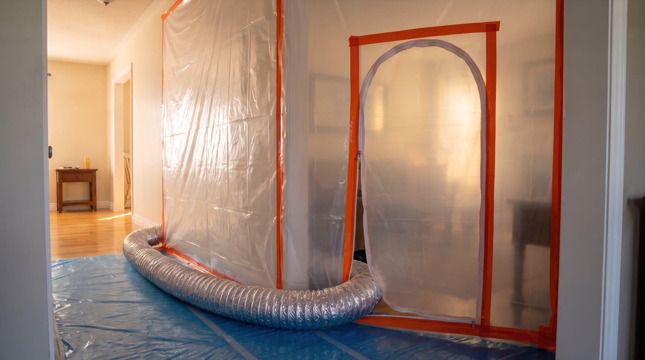 A hallway sealed behind a zippered plastic containment wall with negative-air ducting during mold remediation