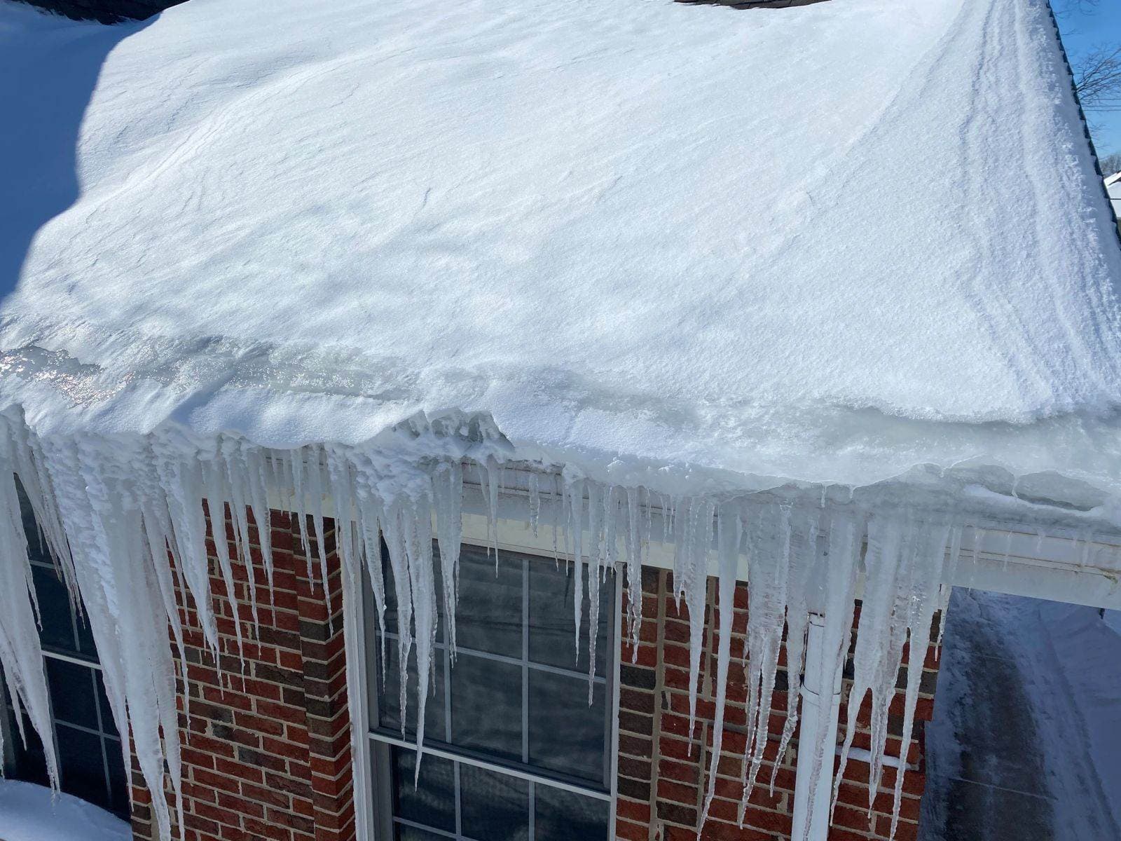 A heavy ice dam and icicles overhanging a brick home before removal