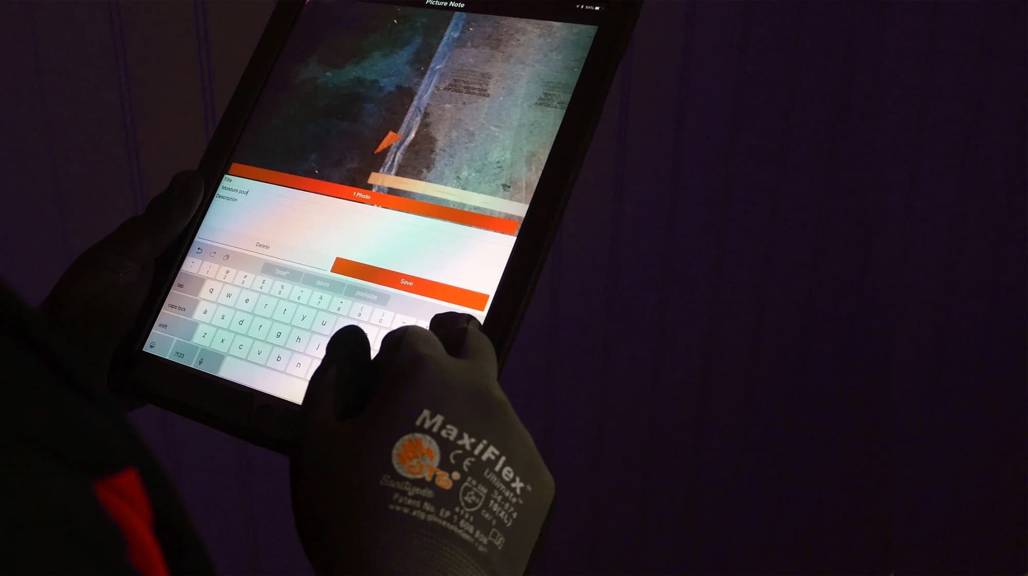 Damage documented on a tablet in gloved hands during a loss inspection
